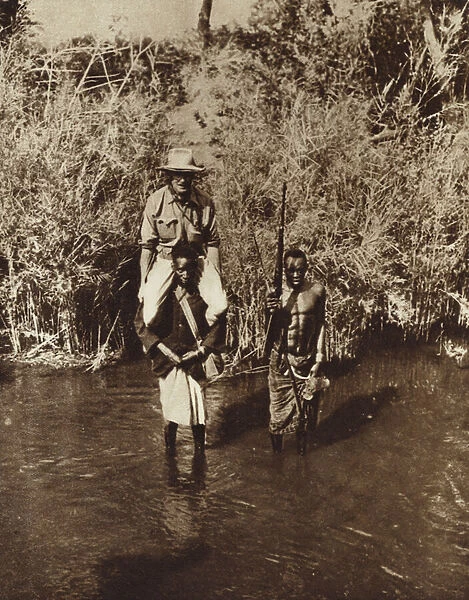 African porter carrying an explorer across the shallow River Nicadgi in Mozambique (b  /  w photo)
