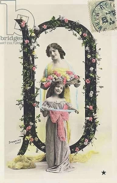 D: Capital letter decorated with flowers, a woman wearing a long cloth, holding a basket of flowers and a girl. 1907 (photograph)