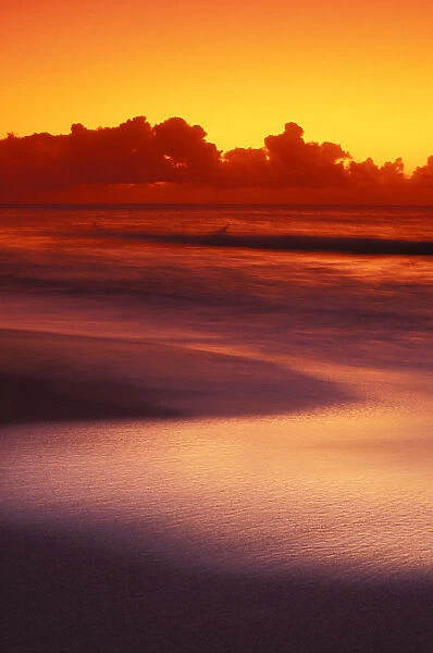 Beach At Sunset With Gentle Wave Rolling In, Dark Orange Sky With Silver Reflections On Water