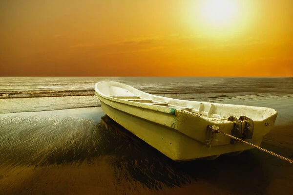 Boat sits on shore with golden sunset