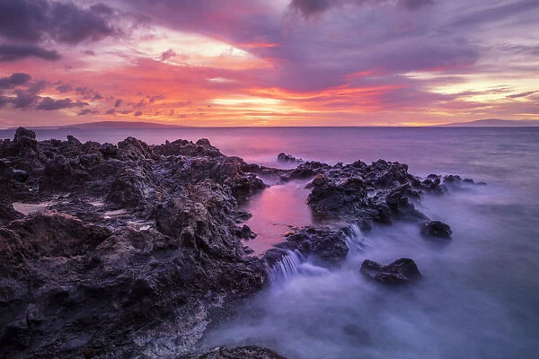 Dramatic sunset over the ocean with waterfalls along the rugged coastline, Wailea, Maui, Hawaii