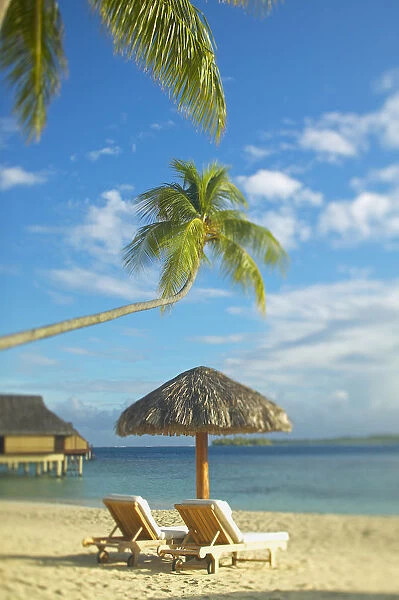 French Polynesia, Tahiti, Bora Bora, Lounge Chairs And Thatch Umbrella On Beach With Tranquil Ocean And Bungalows