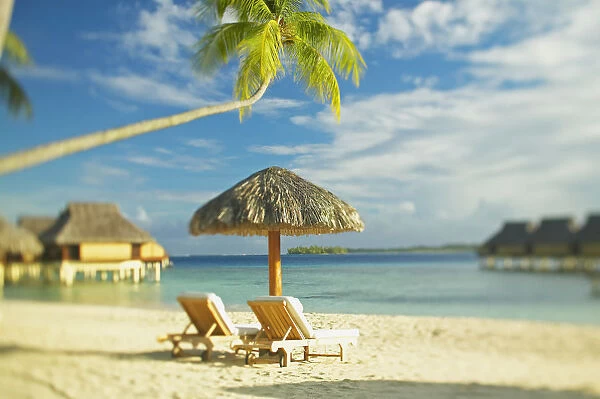 French Polynesia, Tahiti, Bora Bora, Lounge Chairs And Thatch Umbrella On Beach With Tranquil Ocean And Bungalows