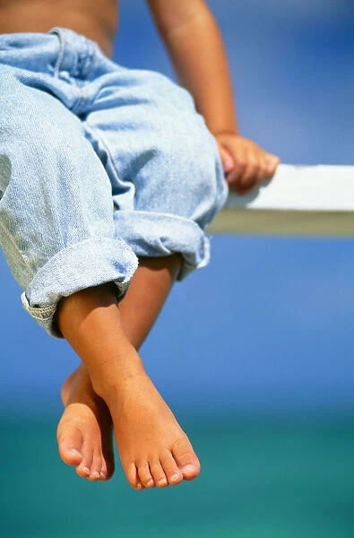 Hawaii, Legs And Feet Of Young Boy Sitting On A Bench By The Ocean