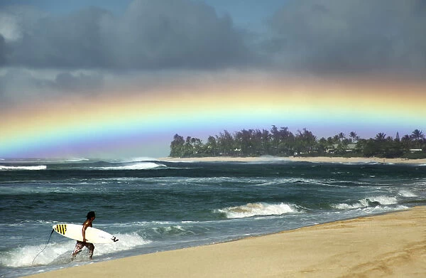 Hawaii, Oahu, North Shore,  /  Nsurfer Exiting Water Admires A Beautiful, Bright Rainbow. Editorial Use Only