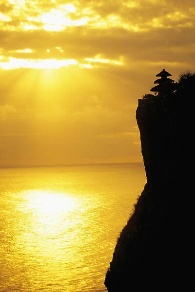 Indonesia, Bali, Uluwatu Temple Silhouetted In Distance Along Cliff, Golden Sunset Reflections On Ocean