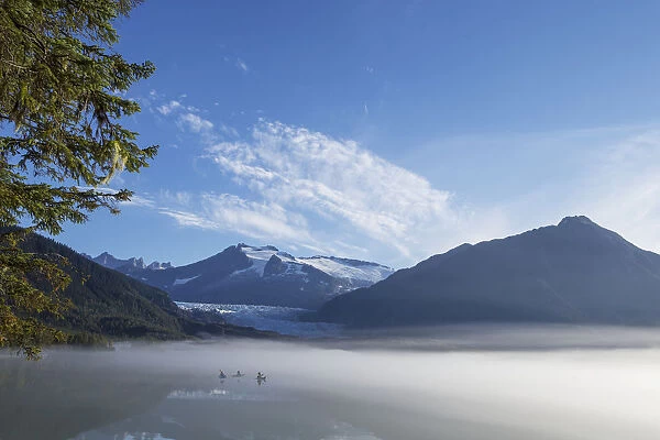 Three Kayakers Paddle The Shoreline Of Mendenhall Lake As Morning Fog Clears, Tongass National Forest, Juneau, Alaska