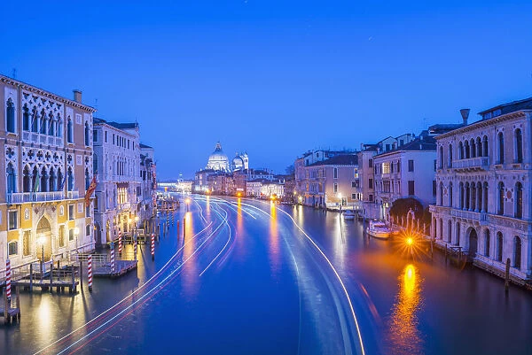 Light Trails On A Canal At Dusk With The Illuminated Salute Church In The Distance; Venice, Veneto, Italy