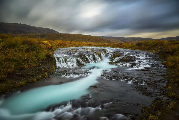 Long Exposure Of Water Flowing Over Rock In A Stream And Dark Clouds In The Sky; Bruarfoss, Iceland