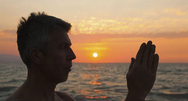 A man in prayer or yoga pose as the sun set on a tropical beach; Puerto vallarta mexico