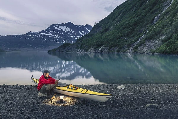 Man Reading On A Electronic Tablet While Camping With A Kayak At Shoup Bay State Marine Park, Prince William Sound, Valdez, Southcentral Alaska