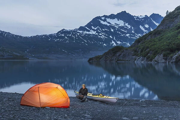 Man Reading On A Electronic Tablet While Camping With A Tent And Kayak At Shoup Bay State Marine Park, Prince William Sound, Valdez, Southcentral Alaska