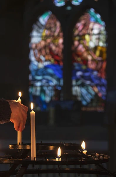 A Mans Hand Lights A Candle In A Church With Colourful Stained Glass Window In The Background; Northumberland, England