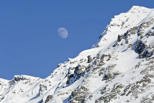 Moon Rising Over Snow Covered Mountain Peak At Hatcher Pass In Southcentral Alaska