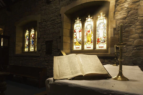 An Open Bible On Display In A Church With Colourful Stained Glass Windows; Bamburgh, Northumberland, England
