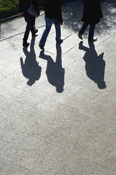 Pedestrians And Their Shadows On A Walkway; Paris, France