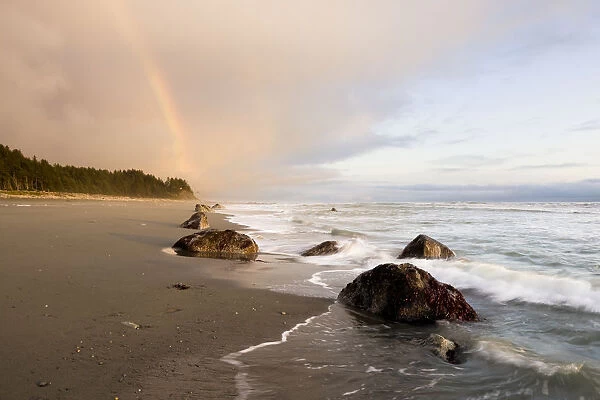 A Rainbow Glows In Storm Clouds Over A Beach And Coastline; Alaska, United States Of America