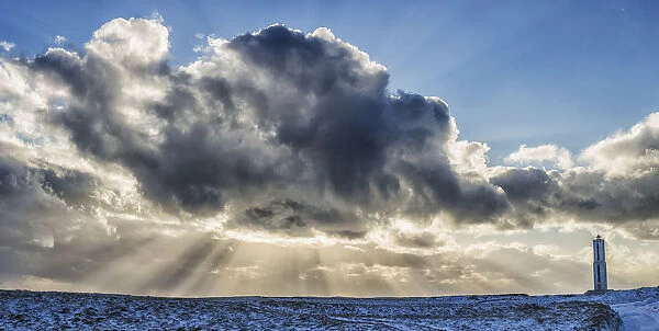 Rays Of Light Shine Out From Behind The Clouds In The Skies Above A Lightnouse Along The Southern Shore Of Iceland; Iceland