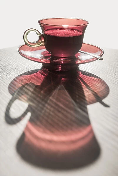 A Red Glass Cup A Saucer With A Beverage Reflected On A White Surface; Locarno, Ticino, Switzerland