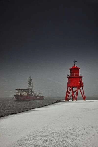 A Red Lighthouse Along The Coast In Winter With A Boat Off The Shore In The Water; South Shields, Tyne And Wear, England