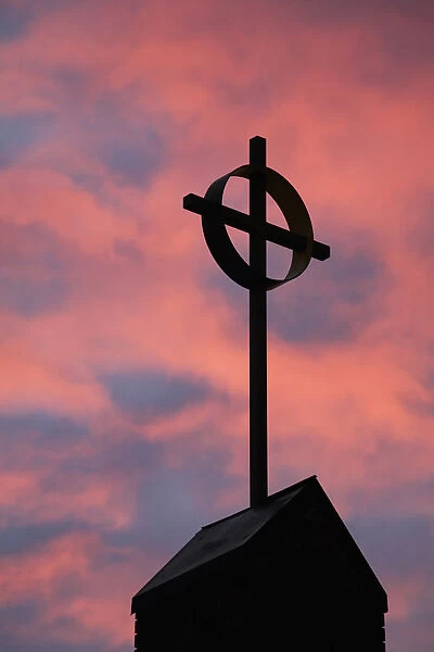 Silhouette of a cross on church steeple with fiery cloud cover in the sky at sunrise; Calgary alberta canada