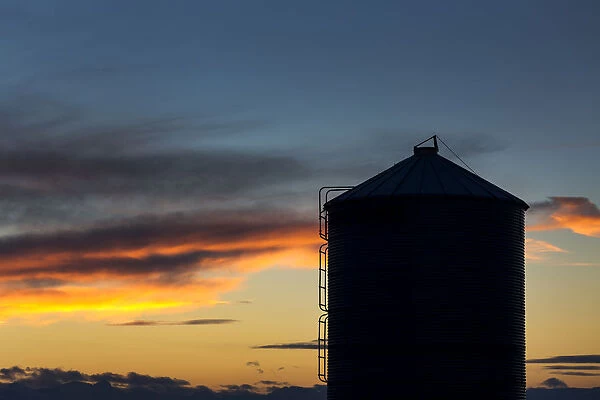 Silhouette Of Large Metal Grain Bin With Colourful Clouds At Sunset With Blue Sky; Alberta, Canada