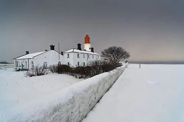 A Snow Covered Fence With A Lighthouse And Building In The Background; South Shields, Tyne And Wear, England