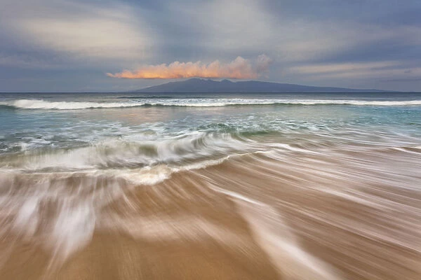 Soft water stretches across the sand at sunrise with a view of Molokai, Maui, Hawaii