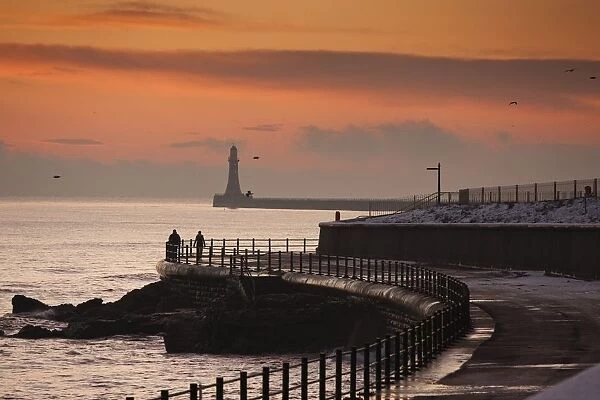 Sunderland, Tyne And Wear, England; People Walking Along The Coast With A Lighthouse In The Distance