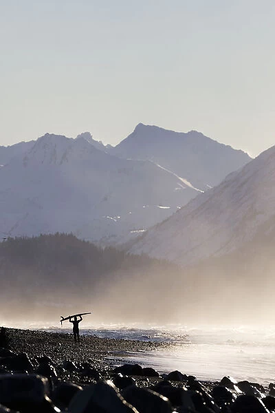 A Surfer Carries Her Surfboard Across The Beach In The Mist Along The Coast; Homer, Alaska, United States Of America