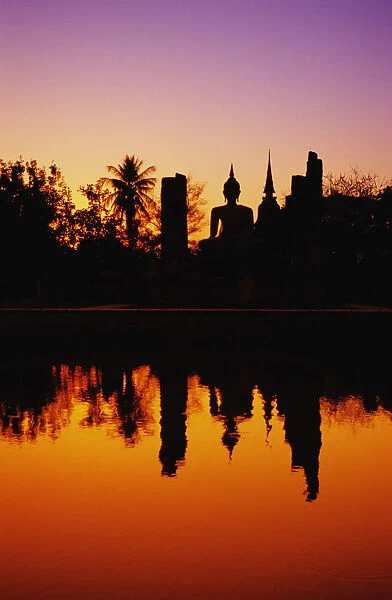 Thailand, Sukhothai, Wat Mahathat, Distant View Of Buddha Statue At Sunset, Silhouetted And Reflecting On Water