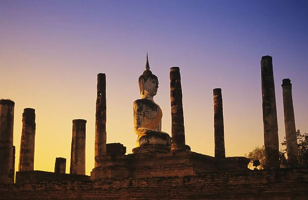 Thailand, Sukhothai, Wat Mahathat, Buddha Statue With Many Pillars At Sunset, Blue And Orange Sky