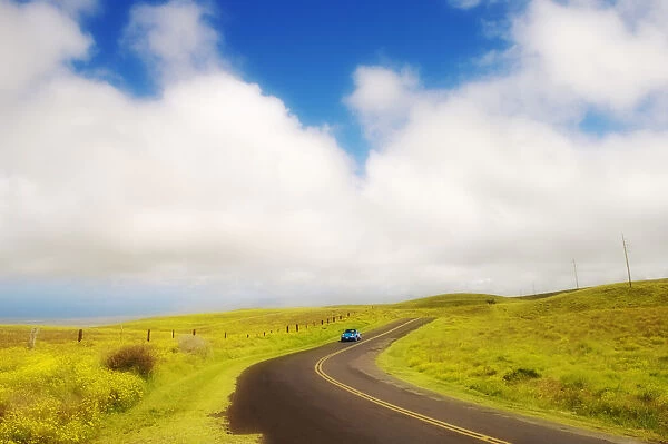 USA, Hawaii Islands, Big Island, Car driving down Saddle Road curving through rolling grass hills near Waikii Ranch; South Kohala