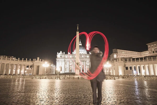 A Woman Stands With A Red Light Trail In The Shape Of A Heart In St. Peters Square; Rome, Lazio, Italy