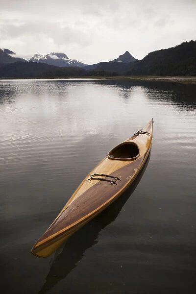 A Wooden Kayak Sits On Tranquil Water With A View Of The Mountains In The Background, Kachemak Bay State Park; Alaska, United States Of America