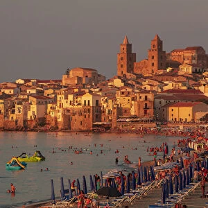 Cefaluaa, Sicily. People under beach umbrellas with the Cathedral in the background at