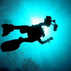 A silhouetted underwater photographer swims at a diving site near the island of Sipadan