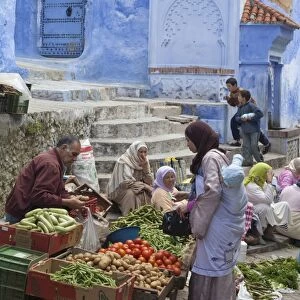 People at market beside blue houses in city, Chefchaouen, Morocco, april