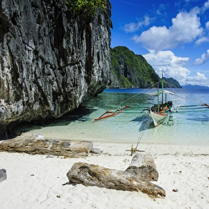 Outrigger boat on a little white beach and crystal clear water in the Bacuit archipelago