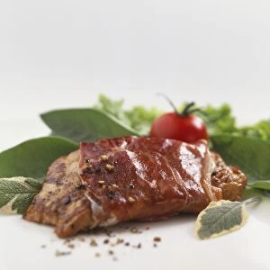 Bacon-wrapped fillet, sprinkled with fresh black pepper, leaves and whole red tomato in background
