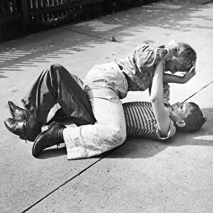 Two young boys fighting on the sidewalk