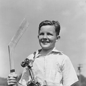 Boy holding hockey stick, metal roller skates hanging on his shoulder, smiling, portrait