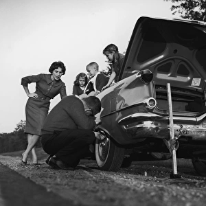 Mother and children (3-8) watching father change flat tire (B&W)