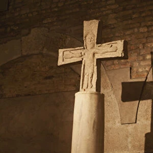 Close up of stone cross / crucifix with a shadow on brick wall in background; Bologna emilia-romagna italy