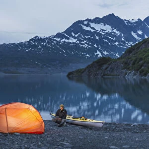 Man Reading On A Electronic Tablet While Camping With A Tent And Kayak At Shoup Bay State Marine Park, Prince William Sound, Valdez, Southcentral Alaska
