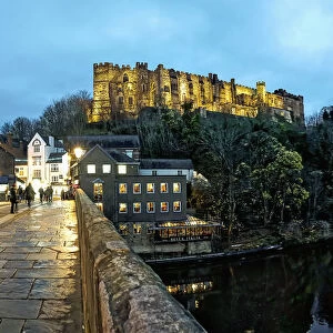 Pedestrians Walking On A Walkway Over A River At Dusk With Durham Cathedral And Castle On A Hilltop; Durham, England