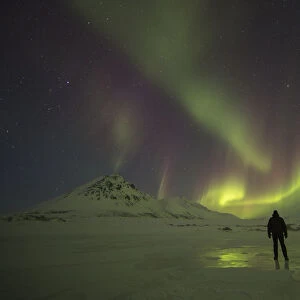 A Person Stands On The Frozen Blackstone River Beneath The Northern Lights; Yukon, Canada