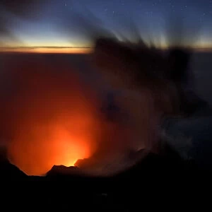 Smoke and ash rise up out of a volcano crater and into the evening sky