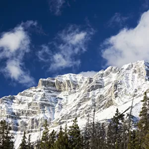 Snow Covered Mountain Peak With Evergreen Trees With Blue Sky And Clouds; Banff, Alberta, Canada
