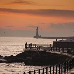 Sunderland, Tyne And Wear, England; People Walking Along The Coast With A Lighthouse In The Distance